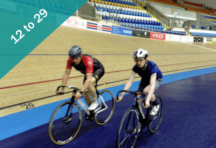 Two people cycling on a velodrome at high speed.