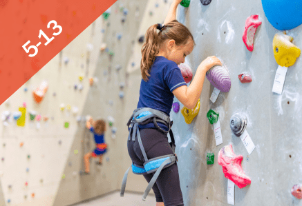 5 to 13. A girl going up an indoor climbing wall in a blue T-shirt.