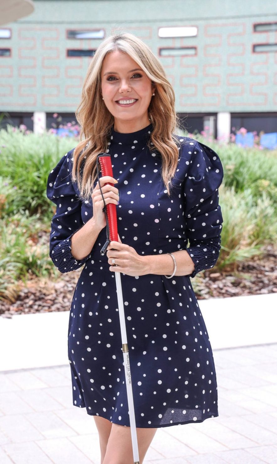 Woman in navy dress with white polka dots holding a white cane and smiling.