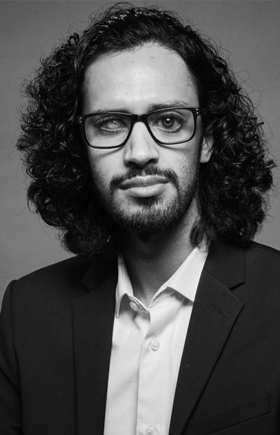 eddie-eyad A black and white photo of Eddie in a suit smiling to camera