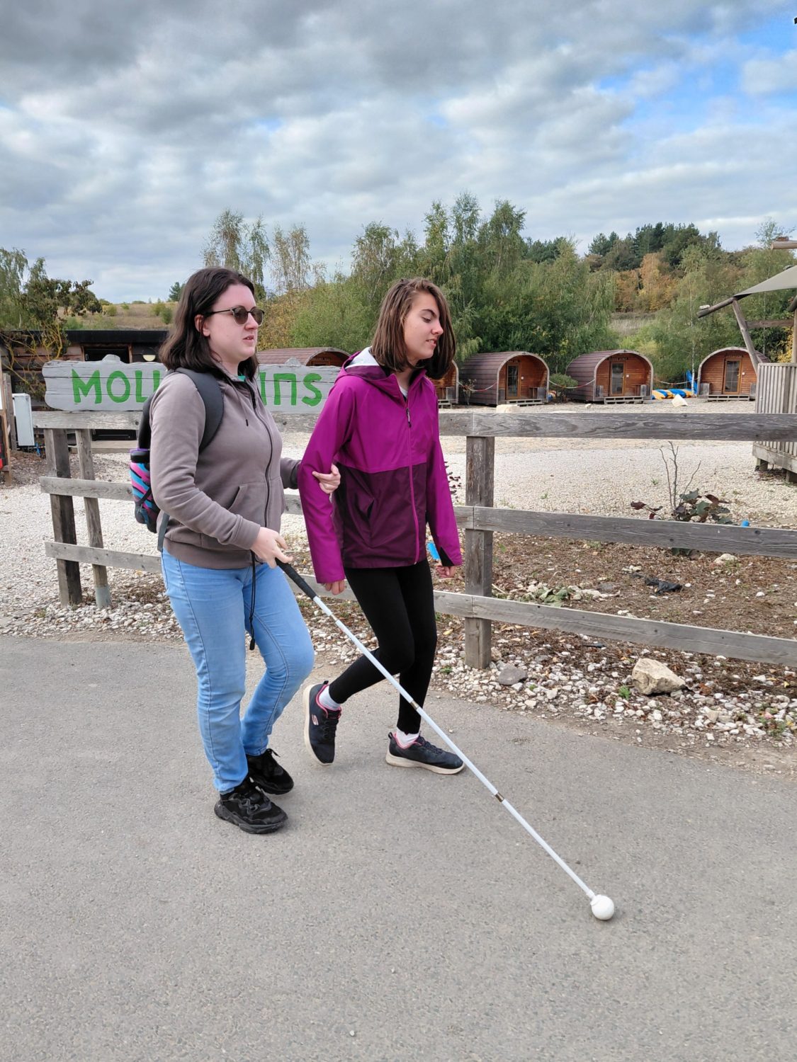 Two teenagers walk together at Summer Camp - one uses a white cane