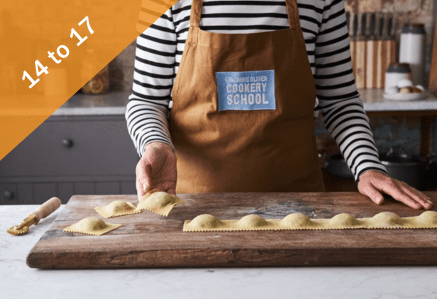 A woman wearing a Jamie Oliver Cookery School apron making pasta.