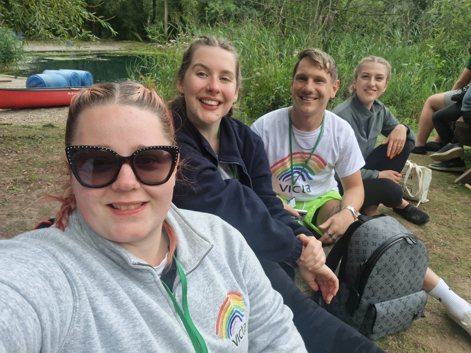 VICTA volunteers smile next to the raft building lake at summer camp
