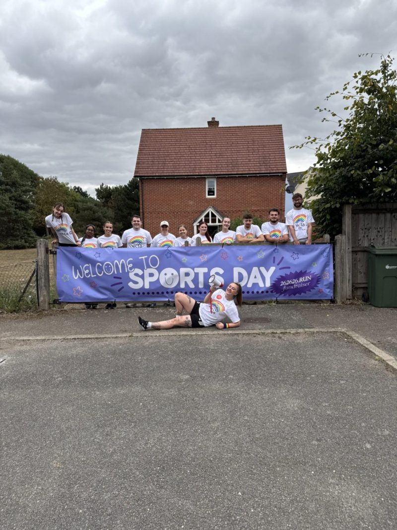 IMG_8006 The group stand behin a Sports Day banner as one person lies in front of it