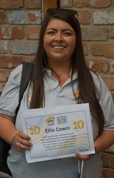 Ellie smiles holding her 10 year volunteering certificate