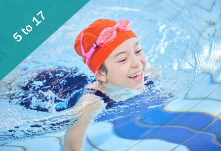 A girl in a red swimming cap in a blue swimming pool smiling.