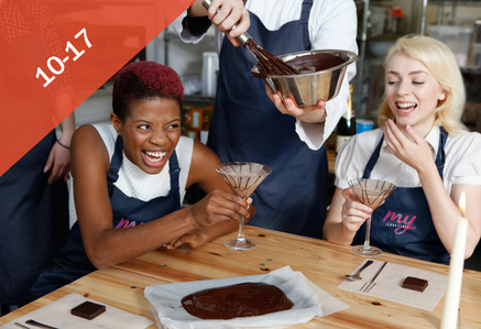 Two women at a wooden table tasting chocolate and laughing.
