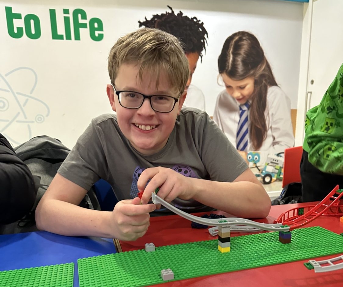 A boy smiles as he builds a Lego rollercoaster track