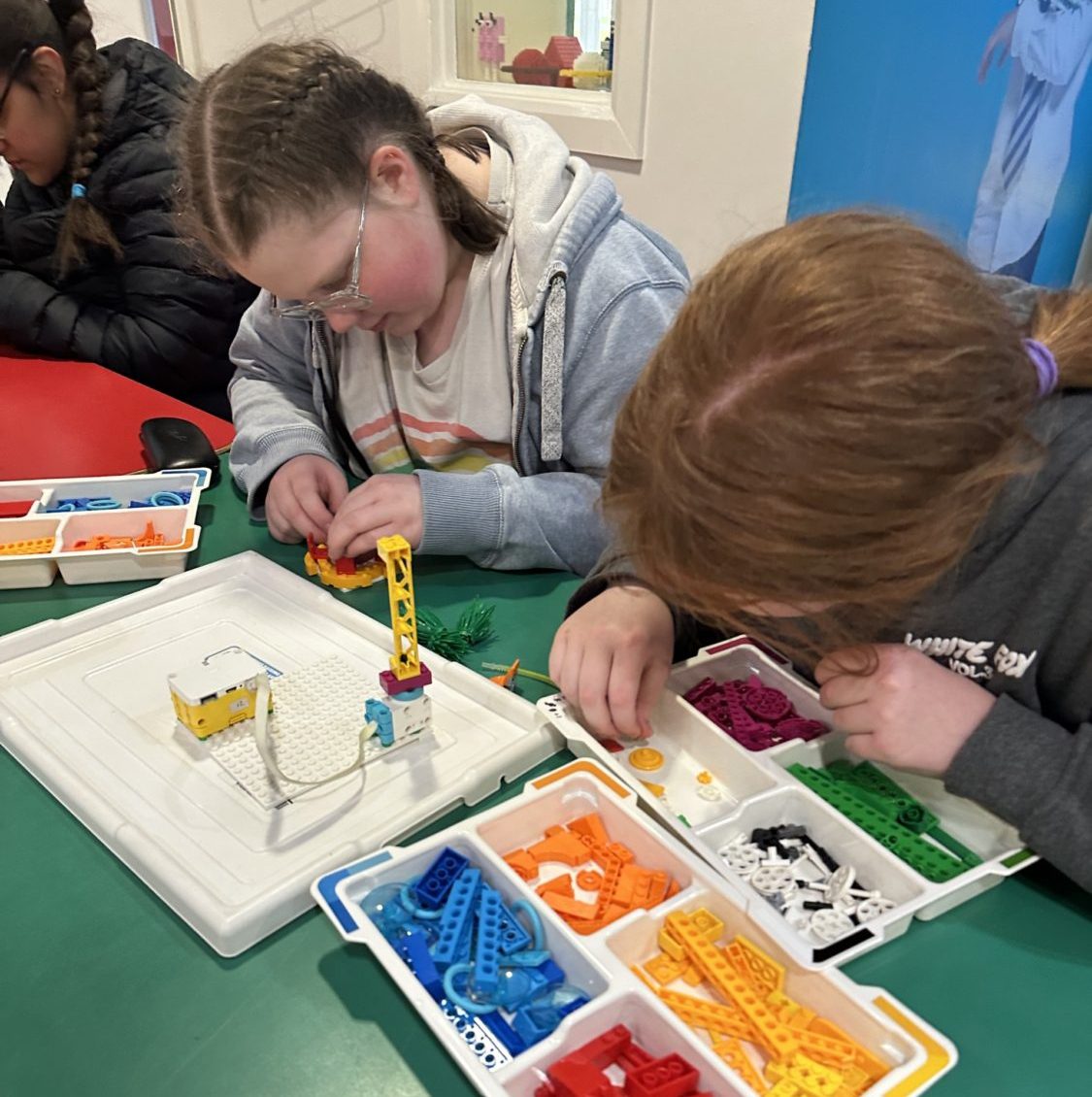 Two girls look closely at Lego pieces in a tray as they build a rollercoaster