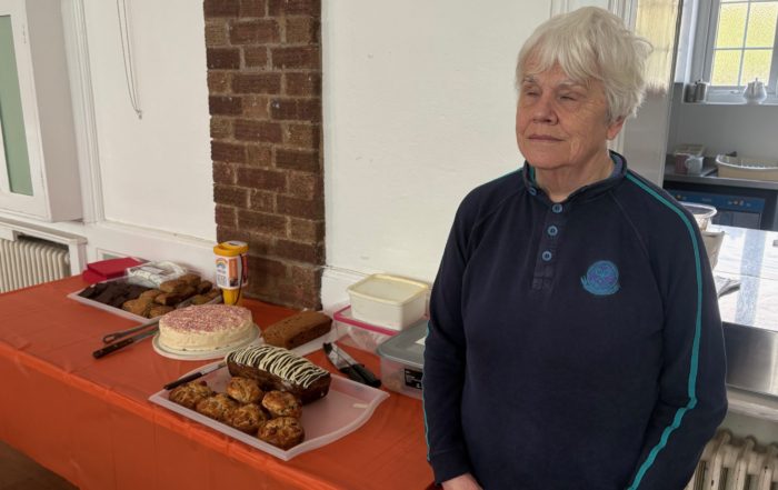 Mary smiles next to the cake table that has a selection of cakes and bakes!