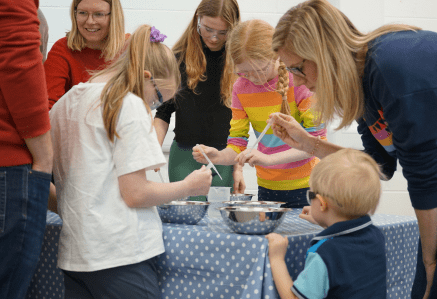 A family gathered around a table conducting a science experiment with pipettes.