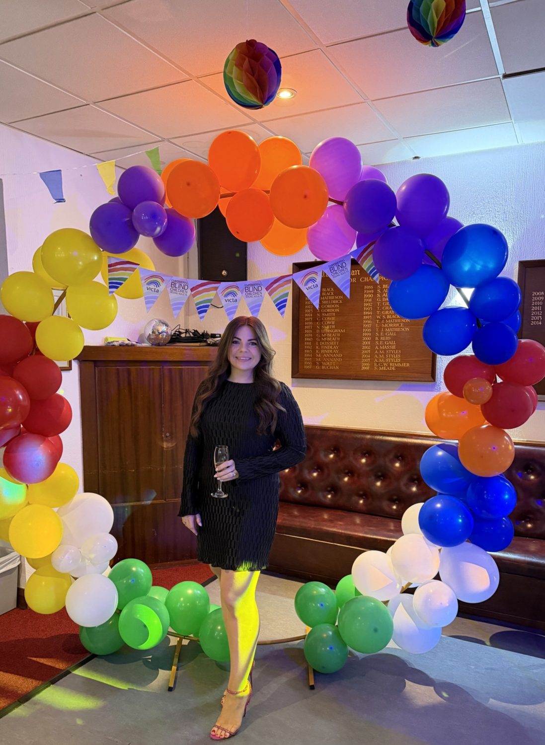 Katie stands in a big rainbow balloon display which is a big circle