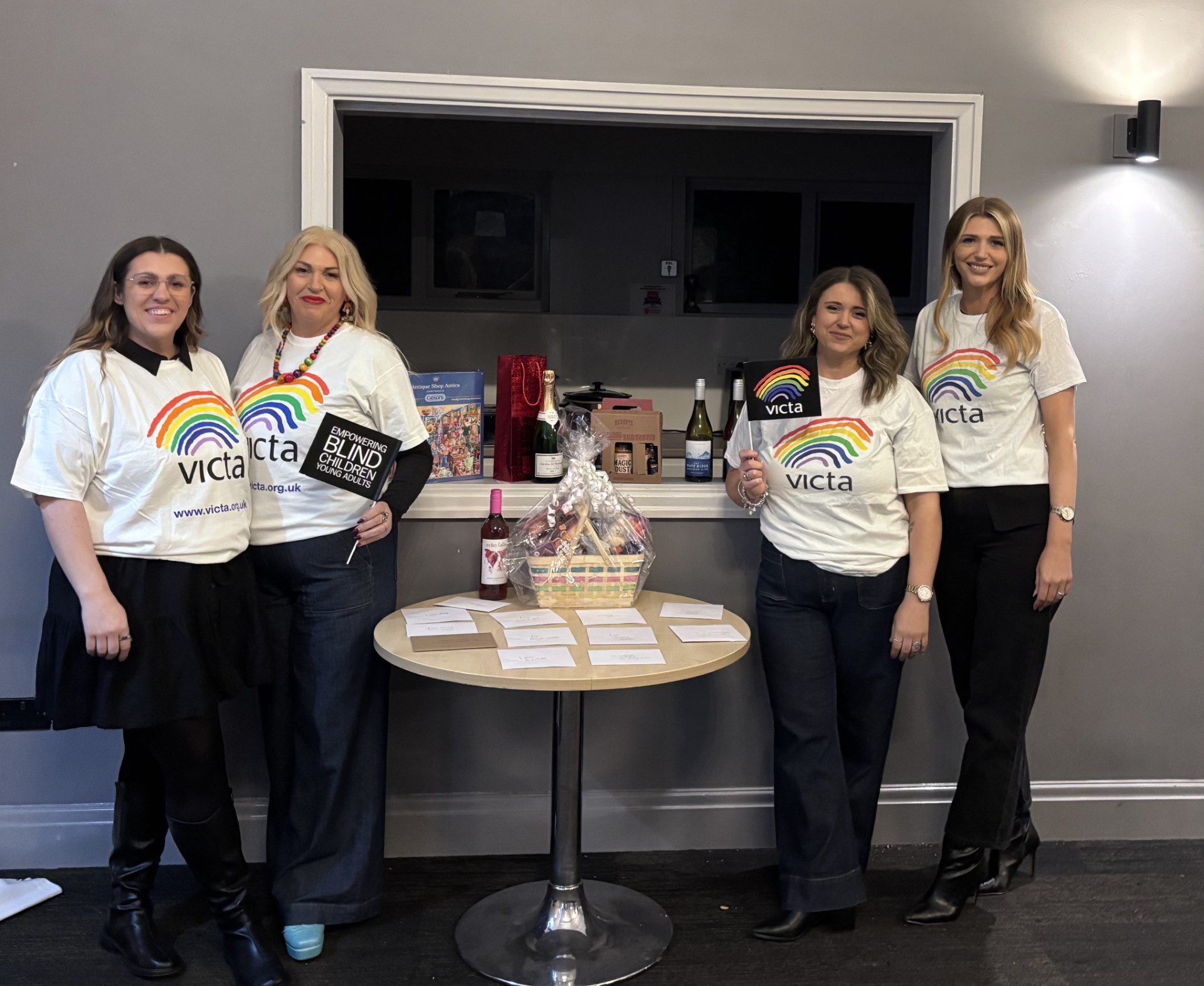 4 fundraisers stand in VICTA t-shirts next to the prize table