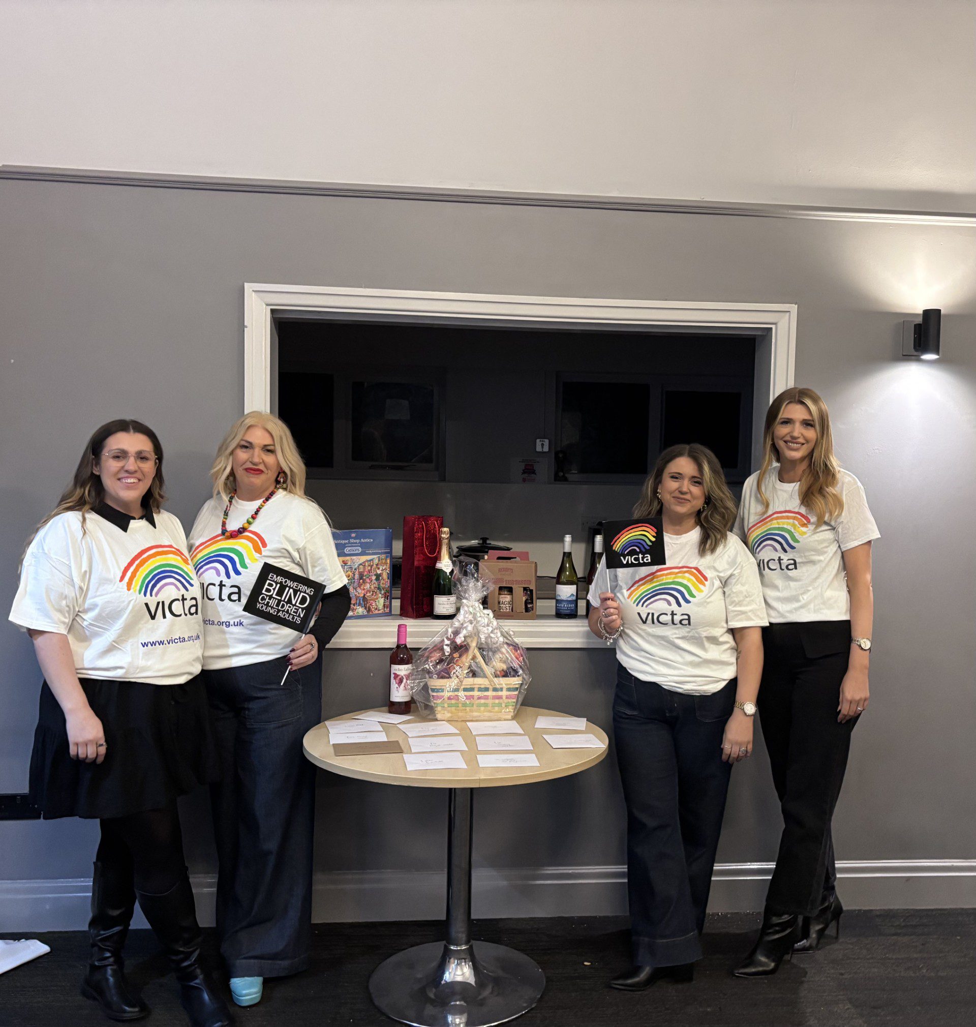 4 fundraisers stand in VICTA t-shirts next to the prize table