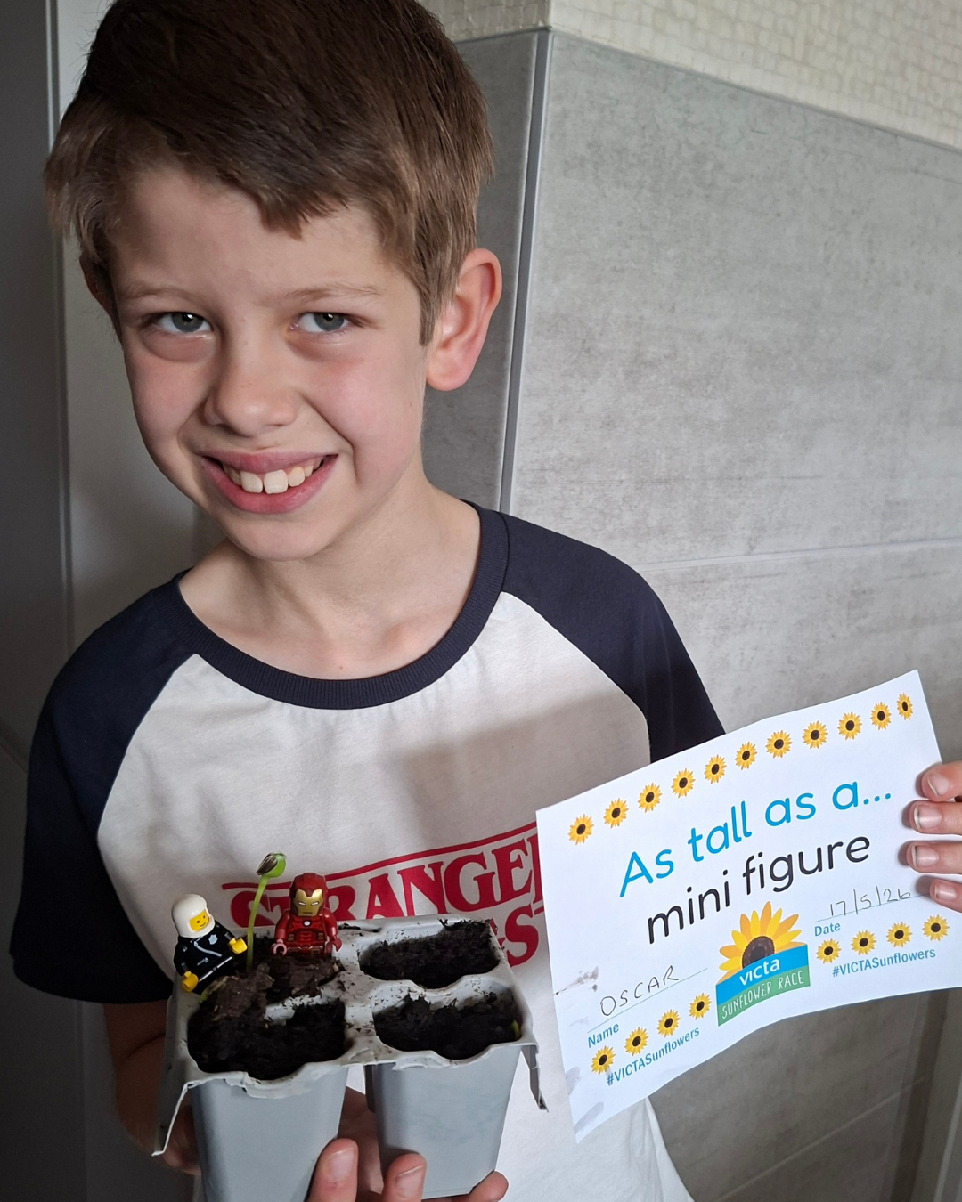 Boy smiling at the camera showing off growing sunflower seedlings.