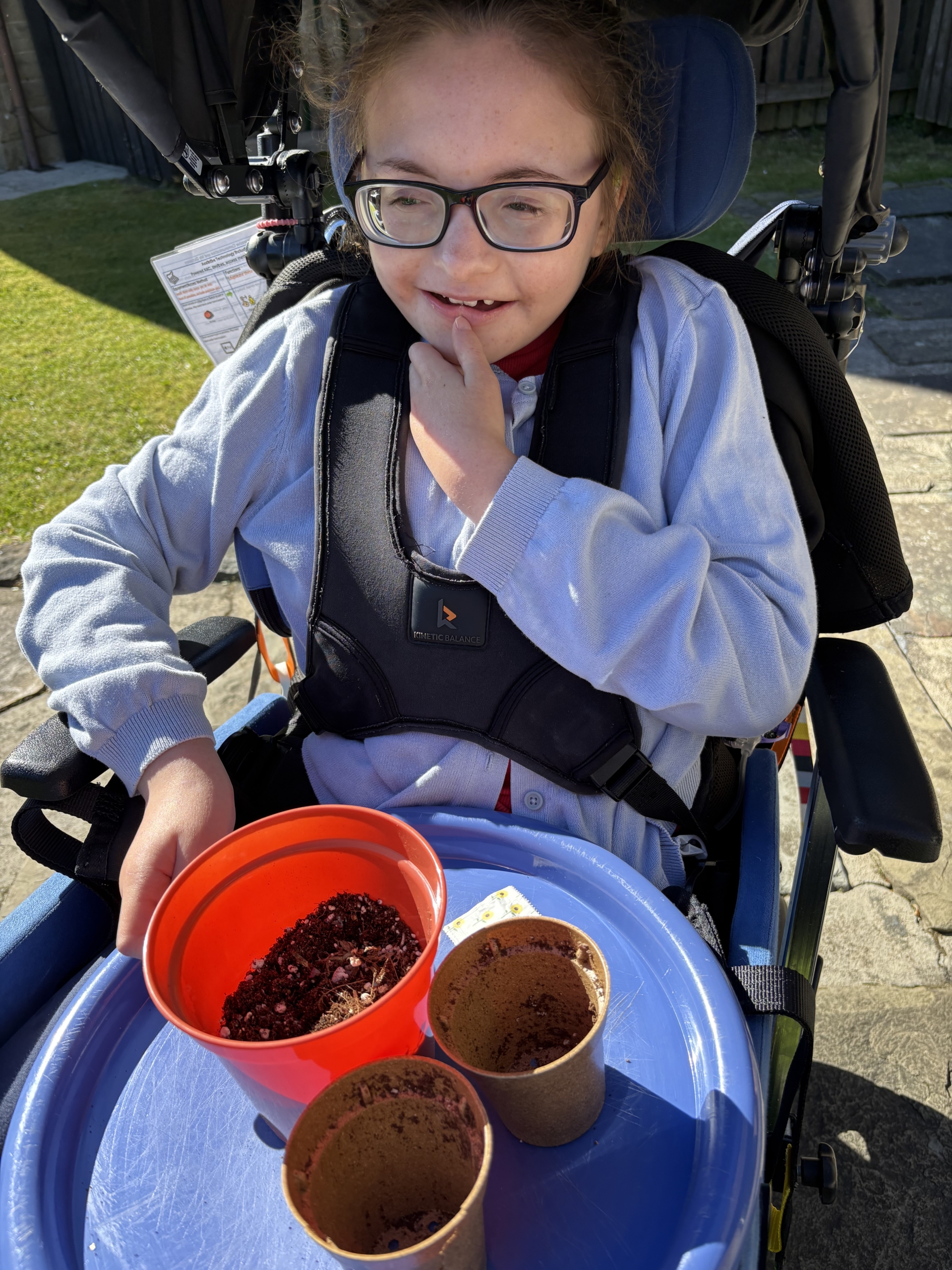 Girl wearing glasses admiring flowerpots containing soil and freshly planted seeds.