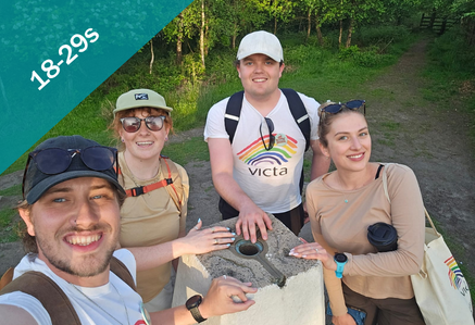 A group of smiling people at a trig point on a hike.