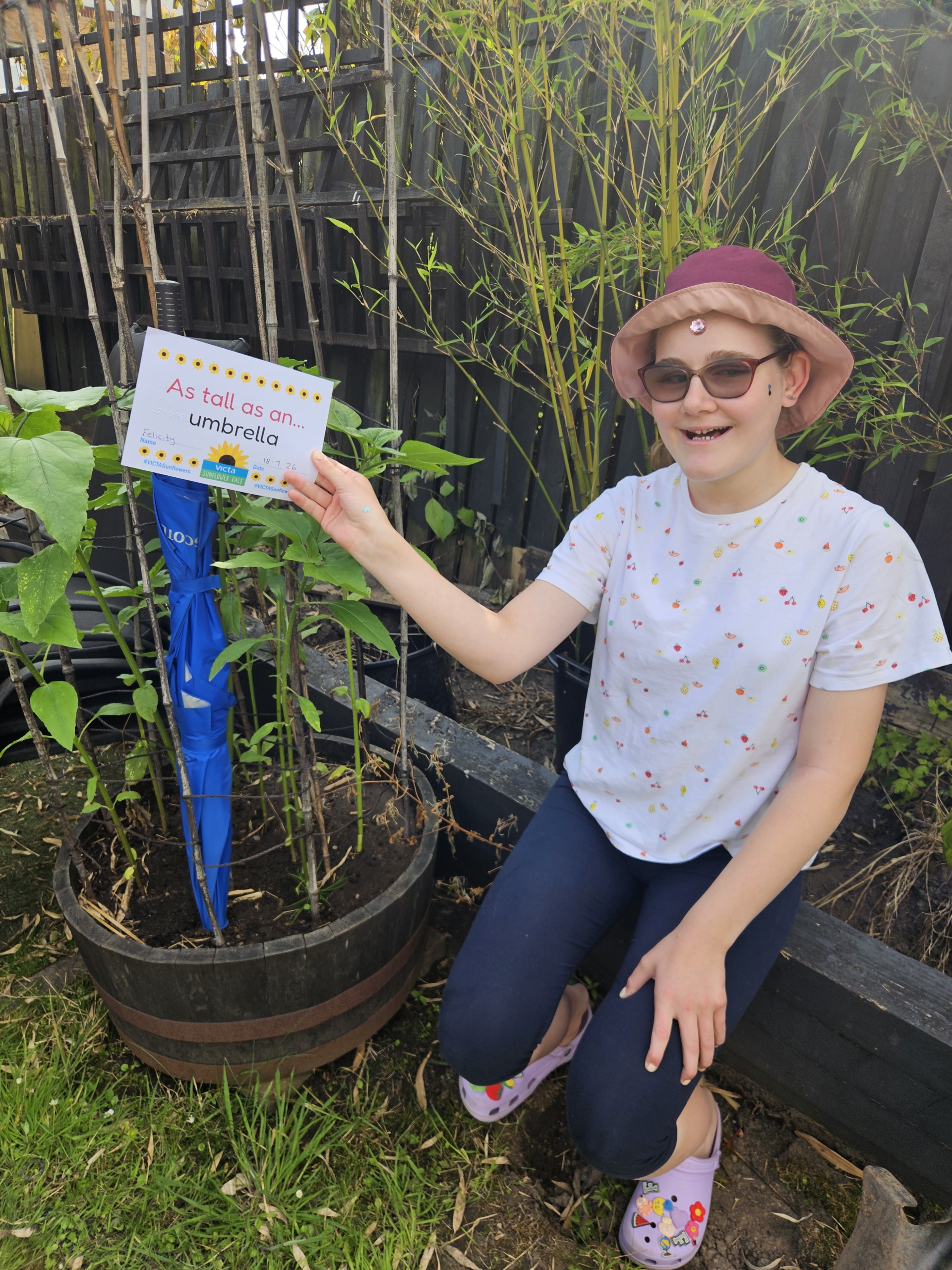Felicity A girl sat outside next to a potted sunflower measured next to an umbrella in height.