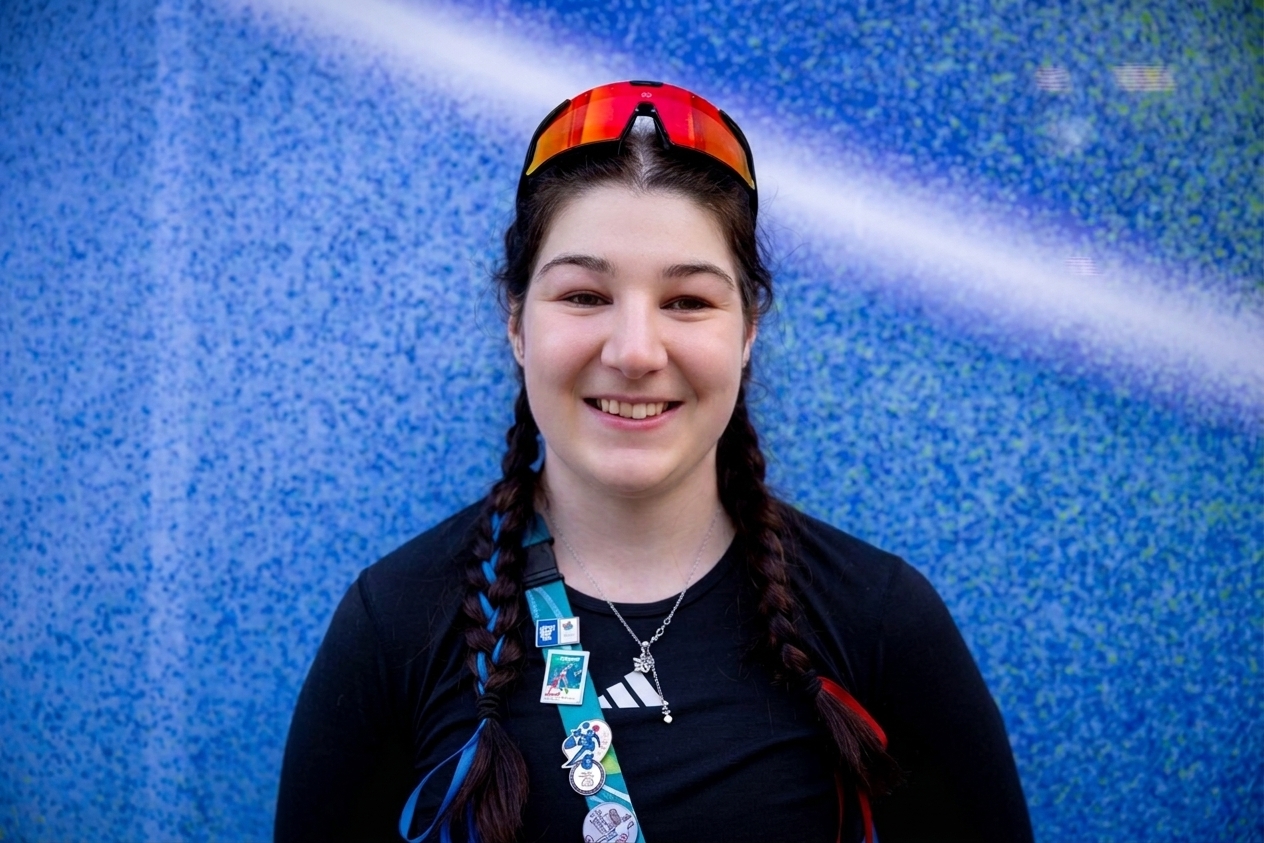 Menna smiles in front of a blue background in sportswear and with ski goggles on her head.